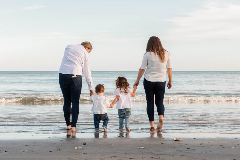 two moms hold daughters hands on beach